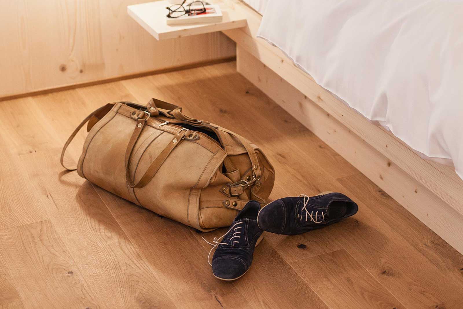 eine Reisetasche und Schuhe liegen am Boden vor dem Bett